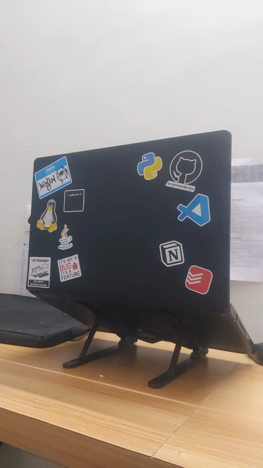 The back of the Dell laptop on a stand, covered in developer stickers including Python, GitHub, VS Code, Notion and Linux.